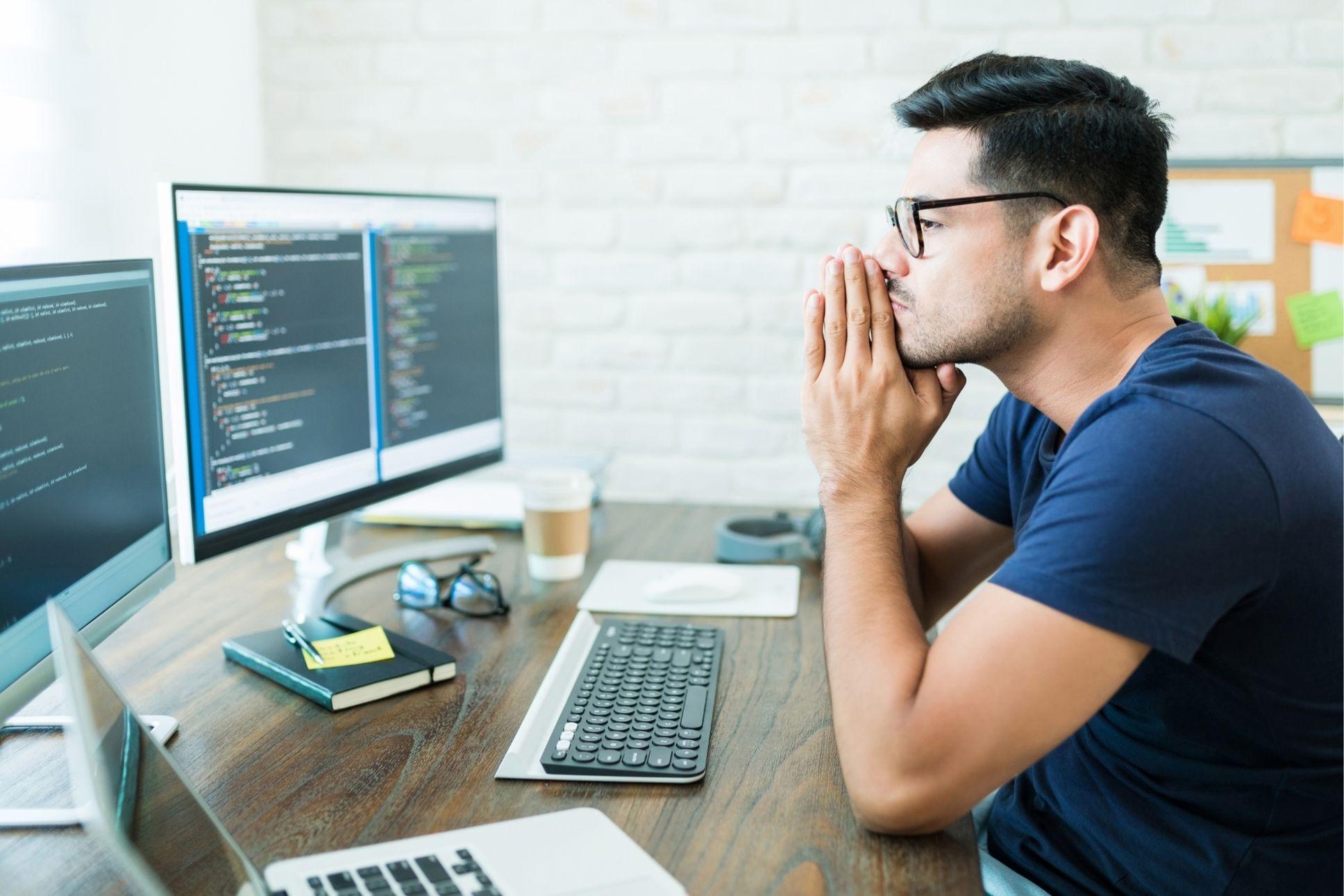 Programmeur qui fait la mise en place d'un logiciel ERP réfléchi devant ses écrans d'ordinateur et son laptop